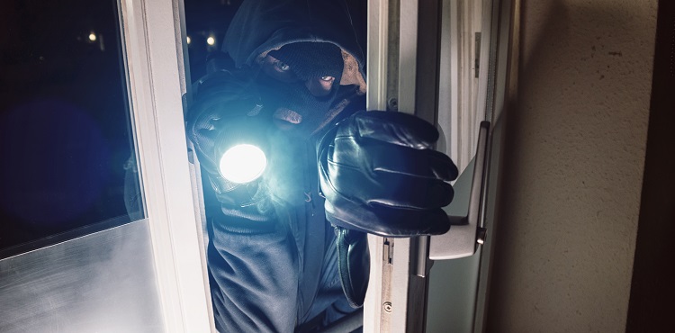 Masked burglar entering amd breaking into a house window with flashlight