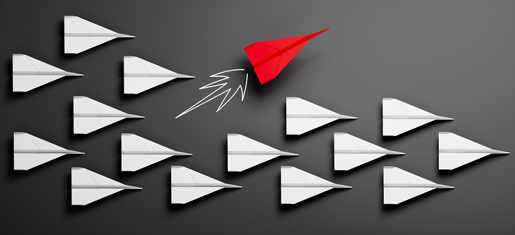 Gruppe von weißen Papierfliegern auf grauem Untergrund mit einzelnem rotem Papierflieger beim Kurswechsel