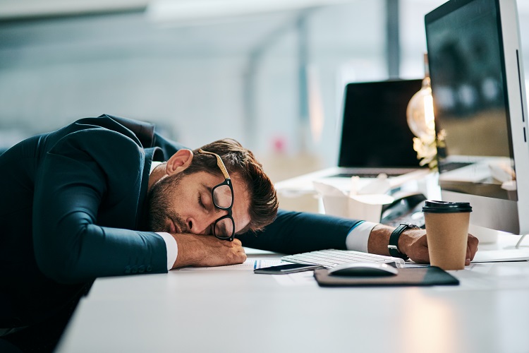 Shot of a tired young businessman sleeping on his desk inside of the office during the day