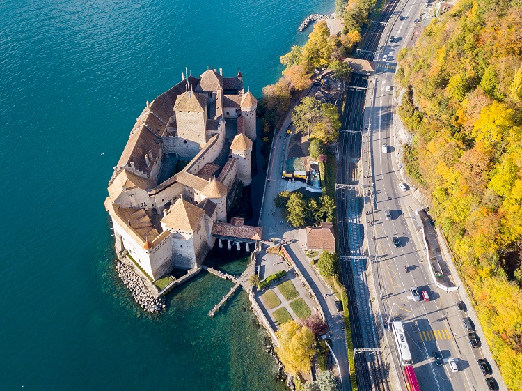 Veytaux, Switzerland - November 01. 2018: Aerial Panoramic View of Chateau de Chillon at Lake Geneva in a golden autumn day, with the Swiss city Montreux at the background